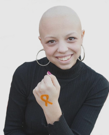 Chica con leucemia tiene un lazo naranja pintado en la mano sonriendo